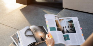 Auf einer Treppenstufe liegen mehrere Magazine, eine Hand hält ein weiteres Heft im Sonnenlicht.