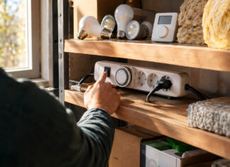 Energie sparen mit Grünspar.de Gründer schaltet Steckdosenleiste im Lagerraum ein, daneben LED-Lampen und Dämmmaterial im Tageslicht