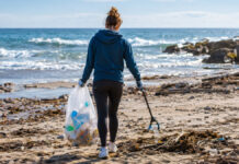Das neue Coach-Feature in der Earnest App: Spielend für eine saubere Umwelt Person sammelt Plastik am Strand in einen transparenten Beutel, Meer im Hintergrund