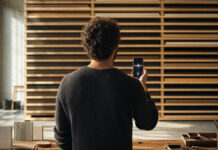 Person von hinten mit Smartphone vor Holzregal in heller Manufakturhalle