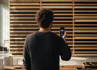 Person von hinten mit Smartphone vor Holzregal in heller Manufakturhalle
