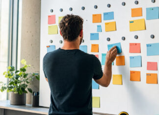 Die 10 besten Projektmanagement-Tools für Startups 2026 Gründer ordnet Projektkarten an einer Magnetwand im Tageslicht