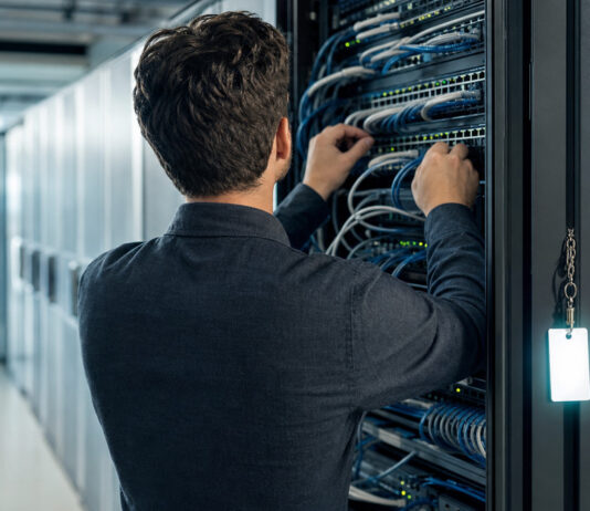 Gründer von hinten vor offenem Serverschrank im Rechenzentrum mit Netzwerkkabeln und Zugangskarte