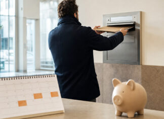 Gründer wirft eine Mappe in einen Wandbriefkasten, daneben Kalender und Sparschwein im Tageslicht.