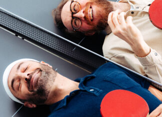 Waldemar Zeiler und Kian Pariwar, die Gruender von Ding Dong Ping Pong, liegen mit Schlaegern auf einer Tischtennisplatte
