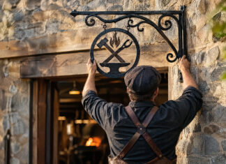 Ein Handwerksmeister montiert ein schmiedeeisernes Zunftschild über dem Eingang seiner neuen Werkstatt
