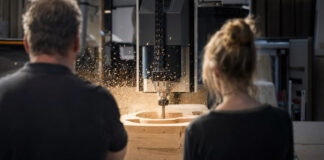 Werkstattmeister und Entwicklerin beobachten in einer Schreinerei eine CNC-Fräse bei der Arbeit