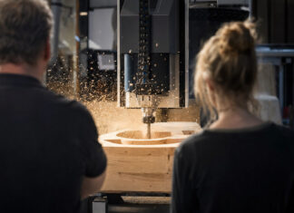 Werkstattmeister und Entwicklerin beobachten in einer Schreinerei eine CNC-Fräse bei der Arbeit