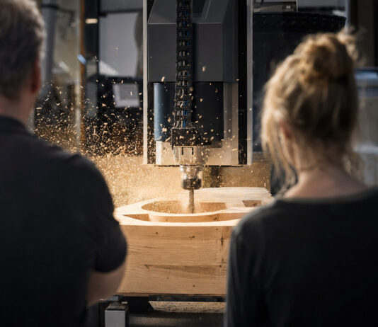 Werkstattmeister und Entwicklerin beobachten in einer Schreinerei eine CNC-Fräse bei der Arbeit