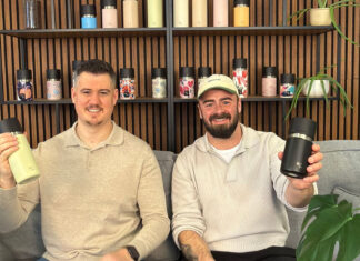 Die zwei IRISgo-Gründer sitzen auf einem grauen Sofa und halten je einen IRISgo-Becher hoch