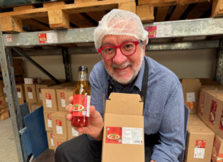 Mann mit Haarnetz hält im Lager eine Flasche Wunderdressing und einen Versandkarton