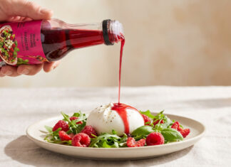 Himbeer-Dressing von Wunderdressing wird aus der Flasche über Burrata mit Himbeeren und Rucola gegossen