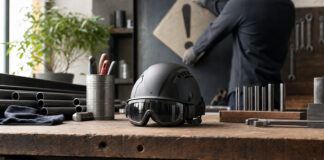 Helm und Schutzbrille auf einer Werkbank, daneben wird ein Warnschild aufgestellt