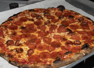 Pizzastueck mit Salami, auf das goldener Hot Honey getraeufelt ist