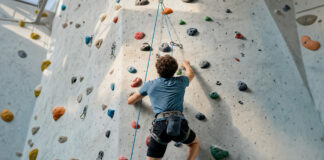 Person klettert von hinten an einer Seilroute in heller Kletterhalle.
