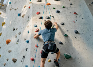 Person klettert von hinten an einer Seilroute in heller Kletterhalle.