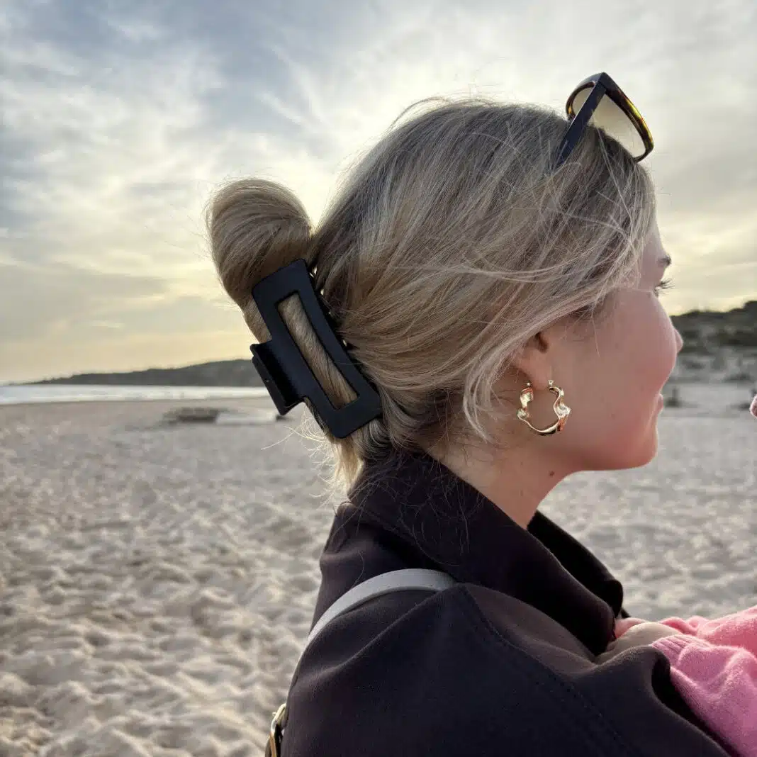 Frau am Strand mit hochgestecktem Haar, eine schwarze ivyclip-Haarklammer haelt den Dutt