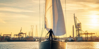 Segelschiff im Hafen mit gehissten Segeln und Person am Bug