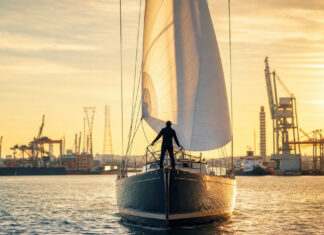 Segelschiff im Hafen mit gehissten Segeln und Person am Bug