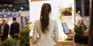 Gründerin am FinTech-Stand mit Smartphone und Kartenlesegerät, von hinten gesehen