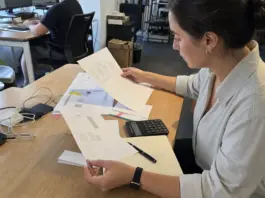 Hände prüfen Freelancer-Rechnungen und Verträge für die Künstlersozialabgabe im Startup.