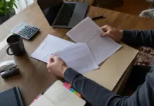 Hände sortieren Steuerunterlagen und Unternehmenskennungen auf einem Schreibtisch.