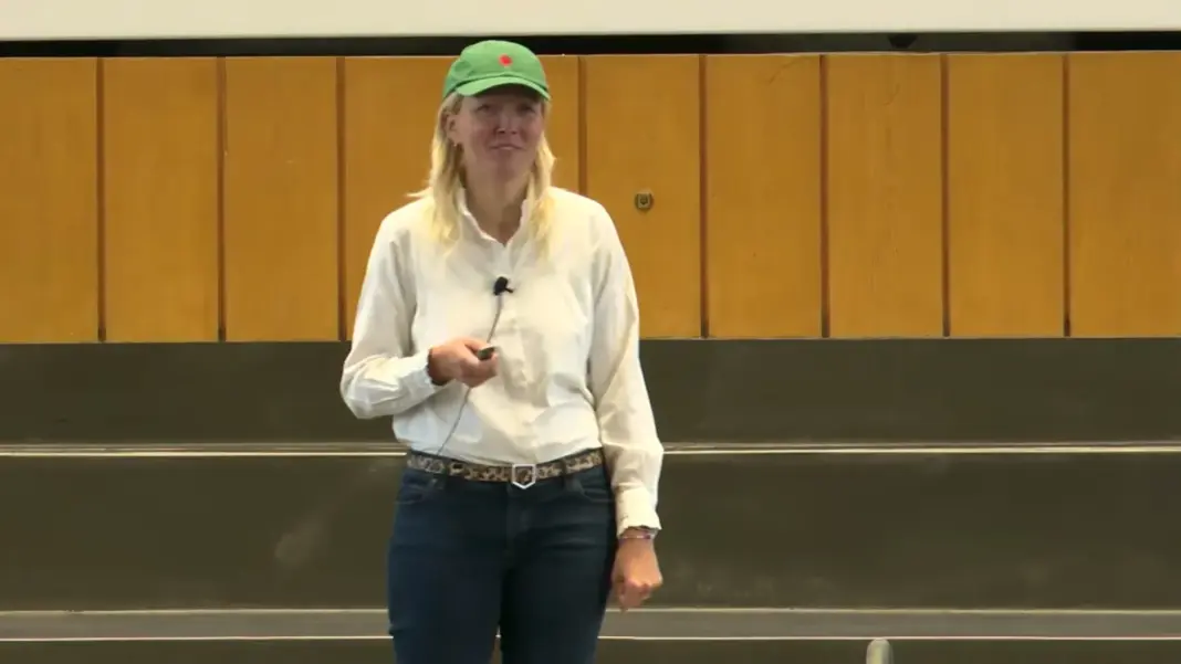 Anna Alex mit grüner Kappe und weißer Bluse hält auf der Bühne des Audimax ihre Keynote mit einem Präsentationsklicker in der Hand