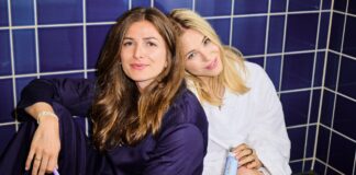 Zwei der Gründerinnen von Artem Oral Care sitzen auf blauen Fliesen, eine mit lila Zahnbürste, die andere im Bademantel mit einem Artem-Produkt