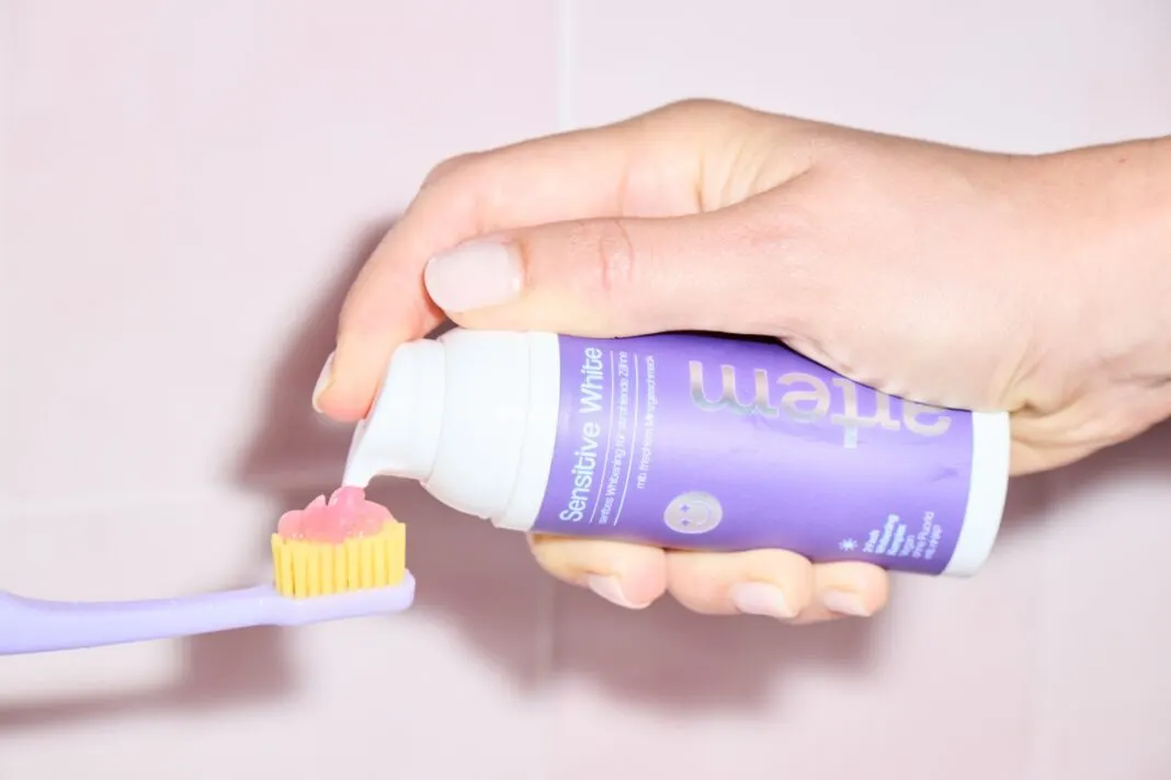 Hand drückt die Zahnpasta Sensitive White von Artem auf eine lila Zahnbürste