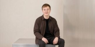 Moritz Zinecker, Gründer von Audecius, sitzt in brauner Jacke auf einem Metallblock vor heller Wand