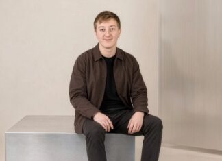 Moritz Zinecker, Gründer von Audecius, sitzt in brauner Jacke auf einem Metallblock vor heller Wand