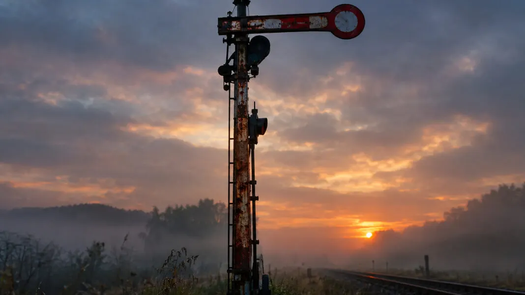 Eisernes Formsignal mit waagerecht gestelltem Flügelarm an einer Bahnstrecke im Abendlicht
