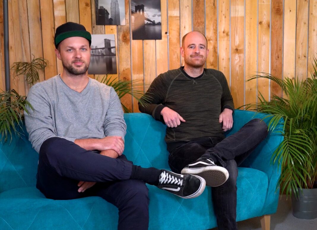 blookery Gründer auf dem Sofa Die beiden blookery-Gründer sitzen auf einem türkisfarbenen Sofa vor einer Holzwand