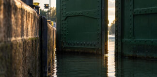 Das Wasser in einer Schleusenkammer steht exakt so hoch wie der Kanal dahinter, das genietete grüne Stahltor öffnet sich einen schmalen Spalt, spätes Nachmittagslicht auf der ruhigen Fläche