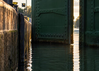Das Wasser in einer Schleusenkammer steht exakt so hoch wie der Kanal dahinter, das genietete grüne Stahltor öffnet sich einen schmalen Spalt, spätes Nachmittagslicht auf der ruhigen Fläche