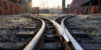 Zwei Schienenstränge einer Feldbahn trennen sich, die beweglichen Stahlzungen liegen blank poliert am rechten Strang an, kaltes Morgenlicht auf dem Stahl