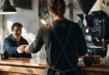 Café-Besitzer reicht einem Stammgast einen Cappuccino über den Tresen