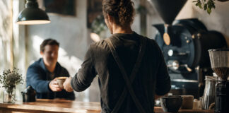 Café-Besitzer reicht einem Stammgast einen Cappuccino über den Tresen
