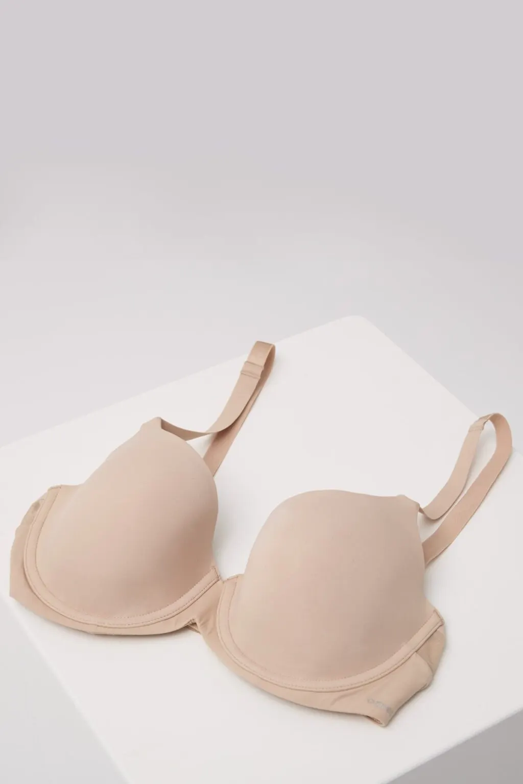 Ein beiger BH von Cupped liegt auf einem weißen Würfel