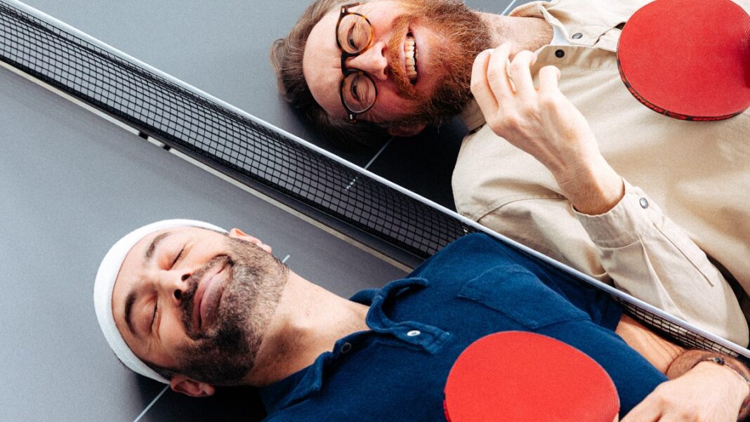 Ding Dong Ping Pong: Waldemar Zeiler und Kian Pariwar, Foto Helmut Sattler Waldemar Zeiler und Kian Pariwar, die Gruender von Ding Dong Ping Pong, liegen mit Schlaegern auf einer Tischtennisplatte