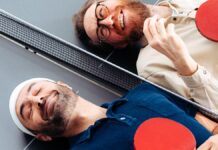 Waldemar Zeiler und Kian Pariwar, die Gruender von Ding Dong Ping Pong, liegen mit Schlaegern auf einer Tischtennisplatte