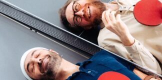 Waldemar Zeiler und Kian Pariwar, die Gruender von Ding Dong Ping Pong, liegen mit Schlaegern auf einer Tischtennisplatte