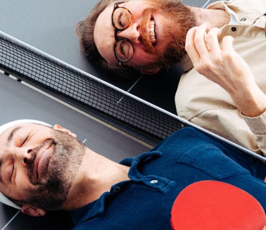 Waldemar Zeiler und Kian Pariwar, die Gruender von Ding Dong Ping Pong, liegen mit Schlaegern auf einer Tischtennisplatte