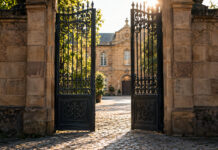Direktvergabe Startups 2026: So nutzt du die 100.000-Euro-Regel beim Bund Ein schweres schmiedeeisernes Hoftor in einer hohen Sandsteinmauer steht einen Spalt offen, dahinter liegt ein gepflasterter Innenhof im warmen Morgenlicht