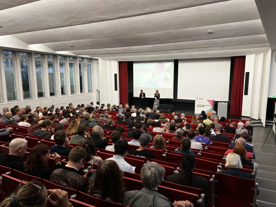 Voll besetzter Hörsaal A im Henry-Ford-Bau von hinten, vorn auf der Leinwand die Ankündigung des Fireside Chats mit Jeannette zu Fürstenberg und Günter Faltin