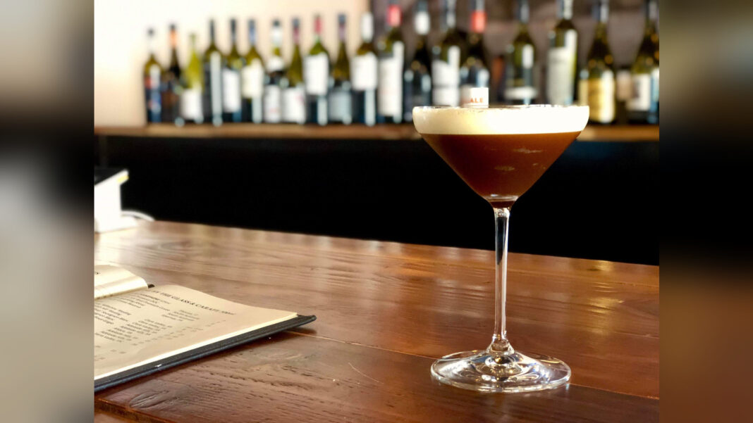 Ein Espresso Martini mit heller Schaumkrone steht auf dem Tresen einer Bar