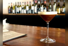 Ein Espresso Martini mit heller Schaumkrone steht auf dem Tresen einer Bar