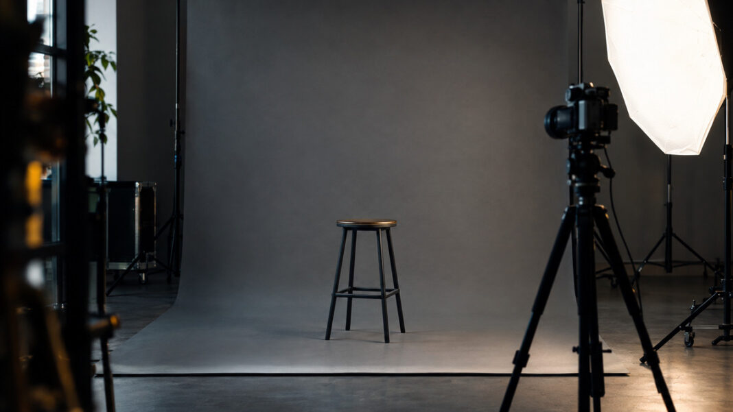 Leeres Fotostudio mit grauem Hintergrund, Hocker, Kamera auf Stativ und Lichtschirm