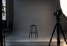 Leeres Fotostudio mit grauem Hintergrund, Hocker, Kamera auf Stativ und Lichtschirm
