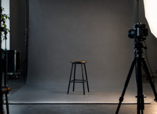 Leeres Fotostudio mit grauem Hintergrund, Hocker, Kamera auf Stativ und Lichtschirm